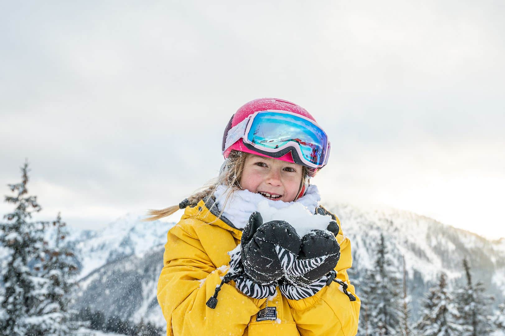 Mädchen mit Skikleidung hält frischen Schnee in den Händen